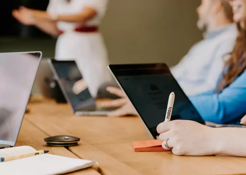 A group of people sitting around a table, laptops in hand, diligently working on digital marketing strategies for their branding agency.